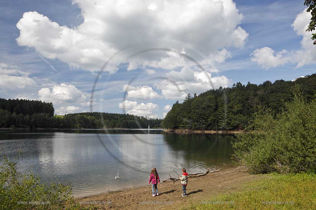 Bevertalsperre mit Landschaft, Segelboot, Kumuluswolken und Spiegelbild. am Seeufer spielende Kinder werfen Steine ins Wasser; Bever dam, lake with sailboat and cumulus clouds with mirror image, playing child at lakeshore are throwing stones into the water