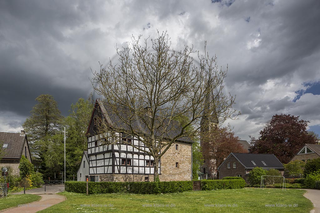 Haarn-Gruiten, Gruiten-Dorf, "Haus am Quall", niederbergische Bauernburg, urspruenglich aus dem 14. Jahrhundert, 1978-1980 rekonstruiert und neu aufgebaut, im Hintergrund die Evangelische Kirche mit dem alten Kirchturm 12. jahrhundert im Fruehling in Wolkenstimmung, Gewitteraufzug; Gruiten-Dorf, village of town Gruiten, "Haus am Quall" and evangelical church in springtime.