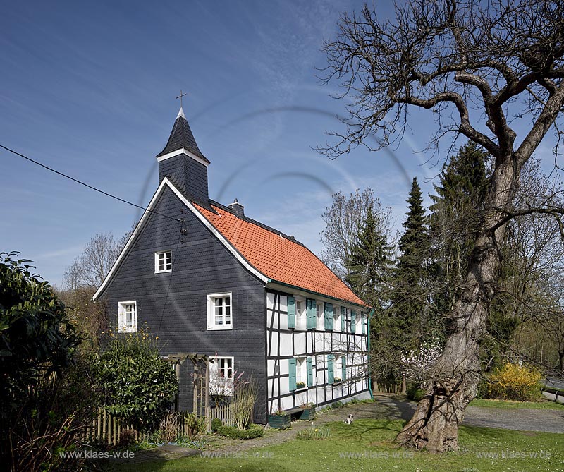 Heiligenhaus-Hetterscheid, Abtskueche. Die 1908/09 erbaute Kapelle war nicht das erste Gotteshaus in der Abtskche. Am Trmchen auf dem direkt nebenan liegenden Fachwerkhaus ist erkennbar, dass dort zuvor eine Kapelle stand. Dieses Fachwerkhaus war 1783 als Schule errichtet worden und hatte 1792 einen Anbau erhalten, der - heute nicht mehr sichtbar  den Hauptschulraum um eine Apsis erweiterte. Dieser erweiterte Raum wurde 1792 als Kapelle eingeweiht; Heiligenhaus Hetterscheid, Abtskueche, halt umbered ofd schoolhouse and chapel in Springime