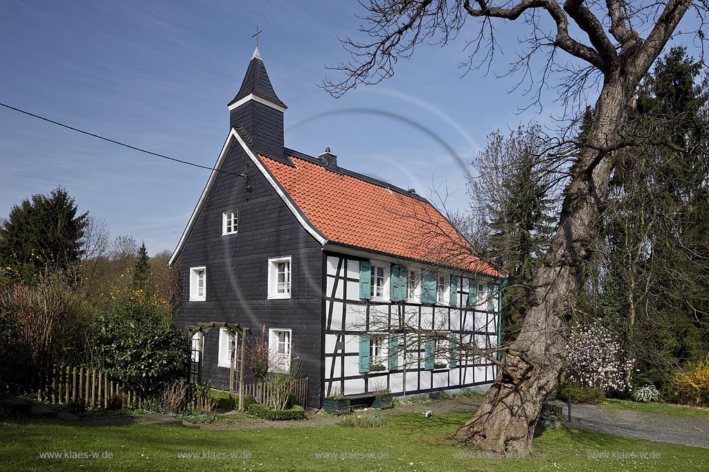 Heiligenhaus-Hetterscheid, Abtskueche. Die 1908/09 erbaute Kapelle war nicht das erste Gotteshaus in der Abtskche. Am Trmchen auf dem direkt nebenan liegenden Fachwerkhaus ist erkennbar, dass dort zuvor eine Kapelle stand. Dieses Fachwerkhaus war 1783 als Schule errichtet worden und hatte 1792 einen Anbau erhalten, der - heute nicht mehr sichtbar  den Hauptschulraum um eine Apsis erweiterte. Dieser erweiterte Raum wurde 1792 als Kapelle eingeweiht; Heiligenhaus Hetterscheid, Abtskueche, halt umbered ofd schoolhouse and chapel in Springime