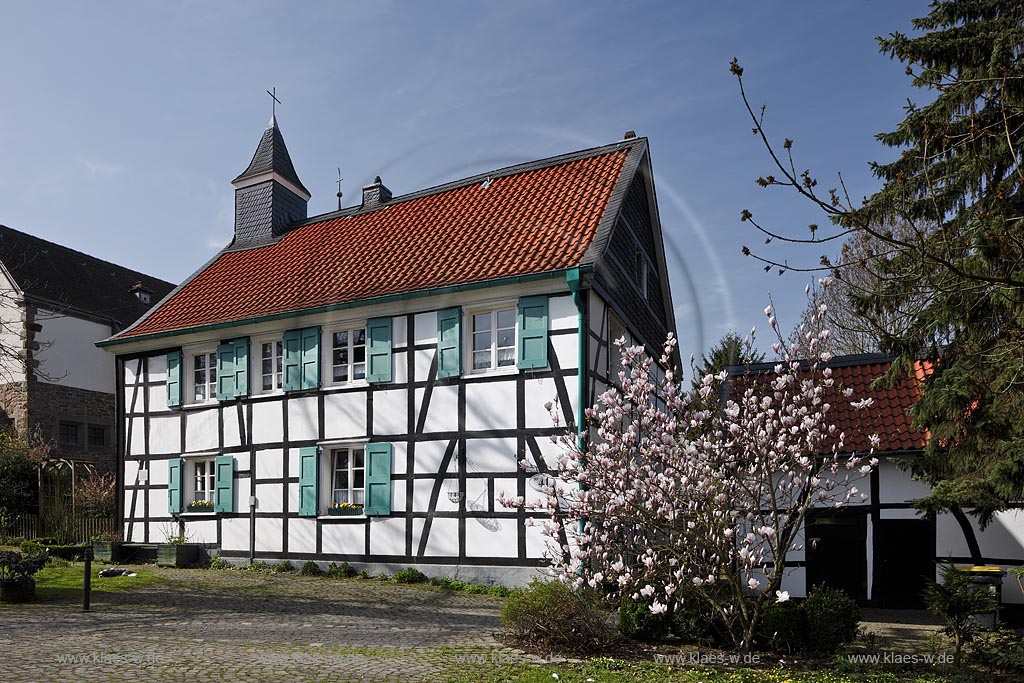 Heiligenhaus-Hetterscheid, Abtskueche. Die 1908/09 erbaute Kapelle war nicht das erste Gotteshaus in der Abtskche. Am Trmchen auf dem direkt nebenan liegenden Fachwerkhaus ist erkennbar, dass dort zuvor eine Kapelle stand. Dieses Fachwerkhaus war 1783 als Schule errichtet worden und hatte 1792 einen Anbau erhalten, der - heute nicht mehr sichtbar  den Hauptschulraum um eine Apsis erweiterte. Dieser erweiterte Raum wurde 1792 als Kapelle eingeweiht; Heiligenhaus Hetterscheid, Abtskueche, halt umbered ofd schoolhouse and chapel in Springime