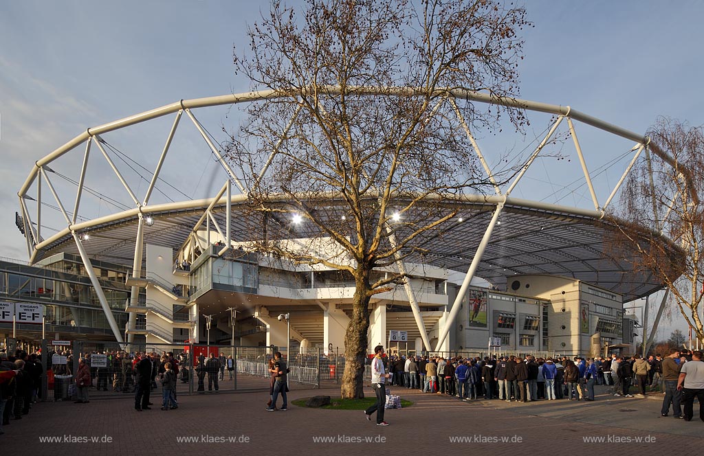Leverkusen Bayarena in abendlicher Beleuchtung der untergehenden Sonne vor einem Fussballspiel von Bayer 04 Leverkusen gegen FC Schalke 04 mit Fans, Zuschauern im Fruehling mit kahlem Baum; Leverkusen footballstadium Bayarena before match with fans in evening sun light
