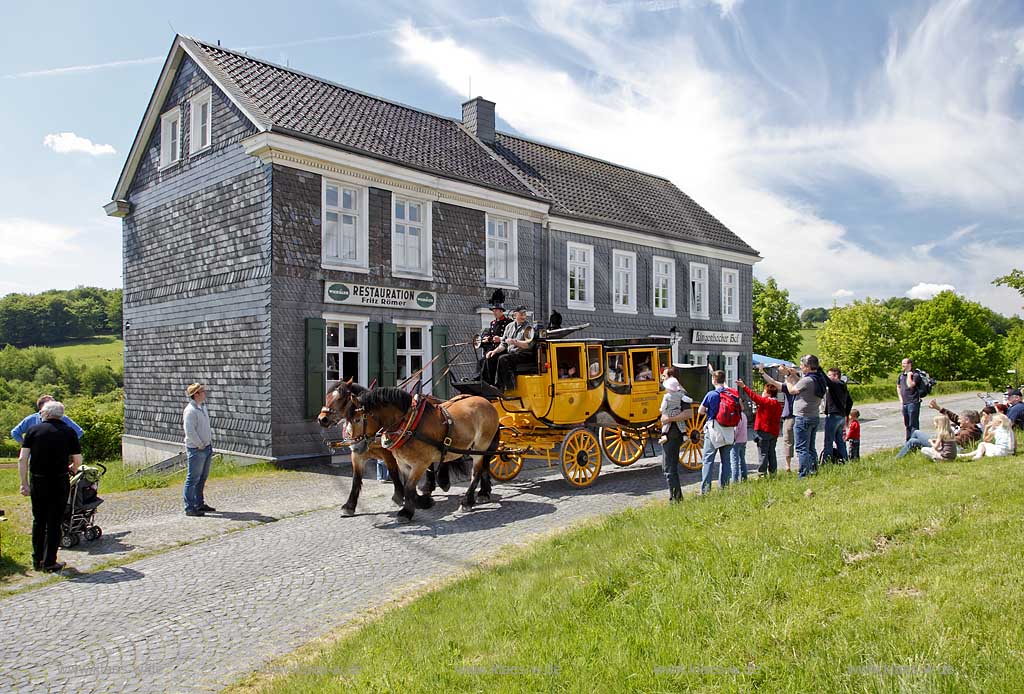 Lindlar Bergisches Freilichtmuseum Lindlar fuer Oekologie und baeuerlich-handwerkliche Kunst, nachgebaute historische Postkutsche, Nachbildung zweispaennig von 2 Kaltblut Pferden gezogen faehrt durch das Museum wahrend der Veranstaltung Jroen und Jedoen Garten und Pflanzenmarkt mit Besuchern,  im Hintergrund die verschieferte historische Fuhrmannskneipe Gaststaette Roemer;  Lindlar open-air museum with replication of a historical stagecoach