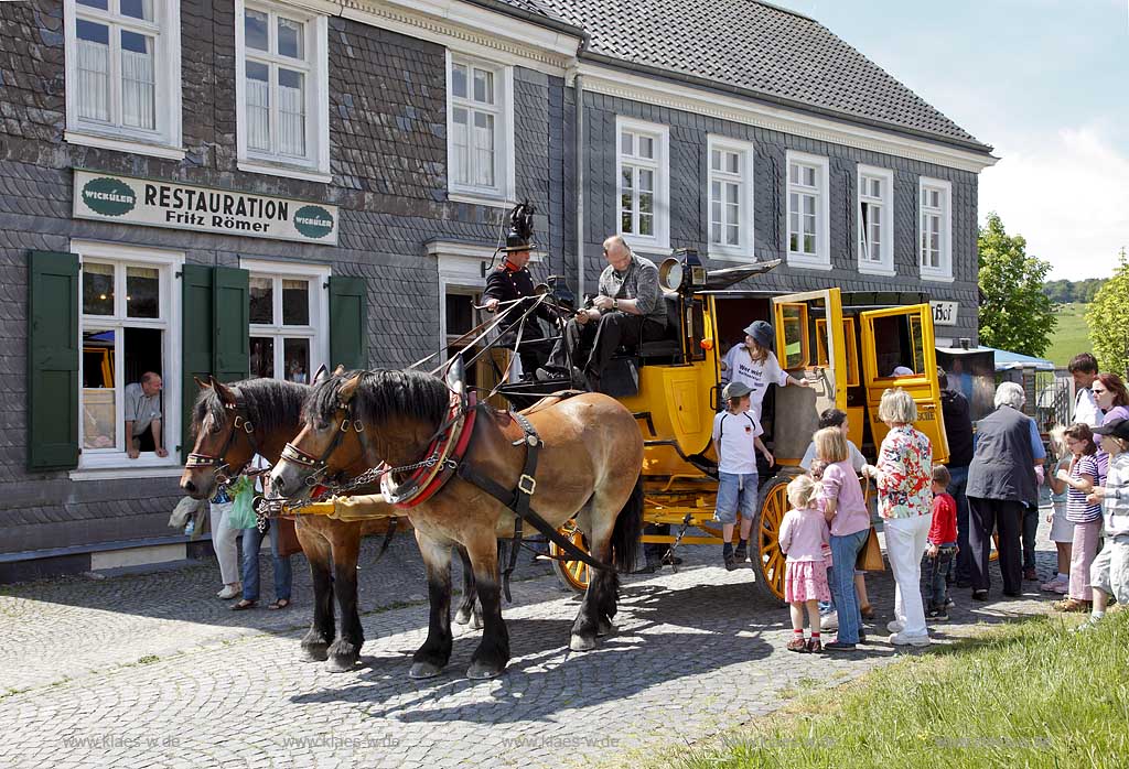 Lindlar Bergisches Freilichtmuseum Lindlar fuer Oekologie und baeuerlich-handwerkliche Kunst, nachgebaute historische Postkutsche, Nachbildung zweispaennig von 2 Kaltblut Pferden gezogen im Museum wahrend der Veranstaltung Jroen und Jedoen Garten und Pflanzenmarkt, im Hintergrund die verschieferte historische Fuhrmannskneipe Gaststaette Roemer, vorne aussteigende Fahrgaeste, Passagiere;  Lindlar open-air museum with replication of a historical stagecoach