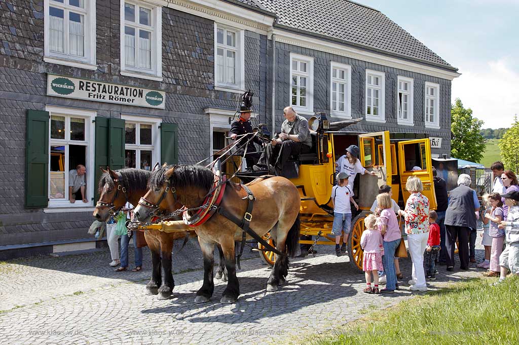 Lindlar Bergisches Freilichtmuseum Lindlar fuer Oekologie und baeuerlich-handwerkliche Kunst, nachgebaute historische Postkutsche, Nachbildung zweispaennig von 2 Kaltblut Pferden gezogen im Museum wahrend der Veranstaltung Jroen und Jedoen Garten und Pflanzenmarkt, im Hintergrund die verschieferte historische Fuhrmannskneipe Gaststaette Roemer, vorne aussteigende Fahrgaeste, Passagiere;  Lindlar open-air museum with replication of a historical stagecoach