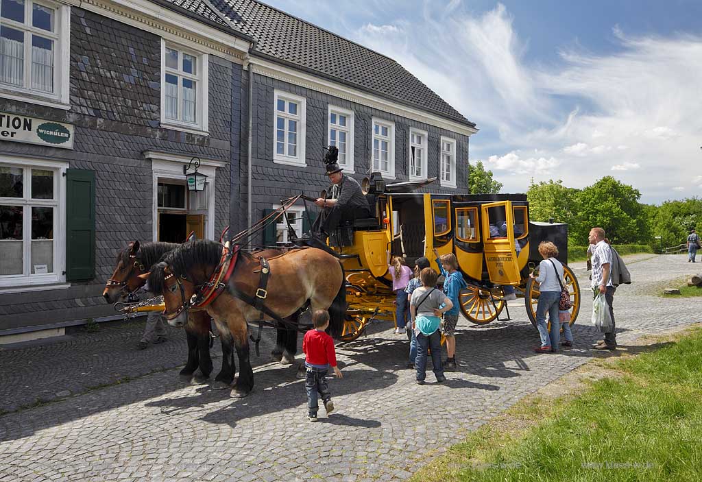 Lindlar Bergisches Freilichtmuseum Lindlar fuer Oekologie und baeuerlich-handwerkliche Kunst, nachgebaute historische Postkutsche, Nachbildung zweispaennig von 2 Kaltblut Pferden gezogen im Museum wahrend der Veranstaltung Jroen und Jedoen Garten und Pflanzenmarkt, im Hintergrund die verschieferte historische Fuhrmannskneipe Gaststaette Roemer, vorne aussteigende Fahrgaeste, Passagiere;  Lindlar open-air museum with replication of a historical stagecoach