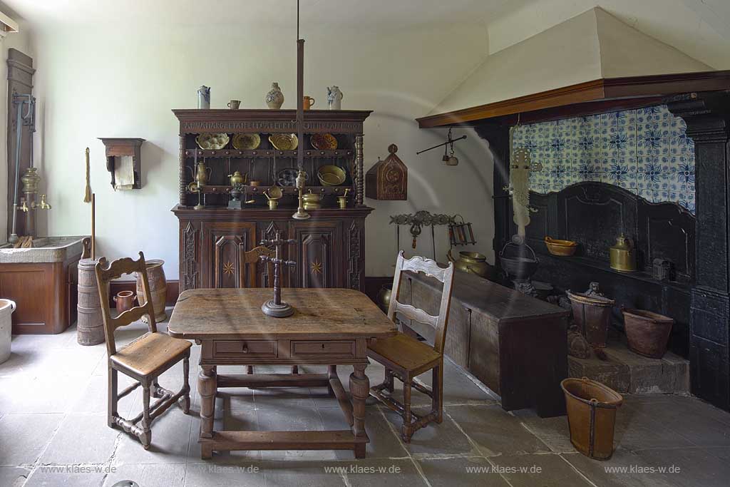 Remscheid Hasten, Haus Cleff, historisches Zentrum, Dauerausstellung in der Kueche mit Fliesenboden und ausgestattet mit antiken Moebeln wie einem Esstisch, zwei Stuehlen, einem grossen Kamin, mehreren Gefaessen, einer Kommode mit jeder Menge Kuchenzubehoer und einem Spuelbecken; Remscheid-Hasten, House Cleff, historcal centre, permanent exhibition in a kitchen with antiquely furniture