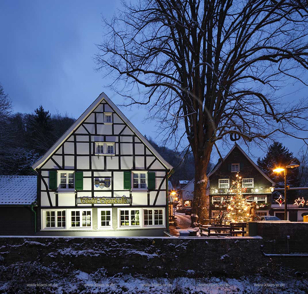 Solingen-Burg, Unterburg Weihnachtliche Stimmung zur blauen Stunde, beleuchteter Weihnachtsbaum, Fachwerkhaus alte Sparkasse, illuminiert und das verschieferte Cafe Meye rmit Burger Brezel auf dem Giebel; Solingen Burg, village Unterburg during Christmas time with Christmas tree and old half timbered bankhouse Sparkasse, illiminated