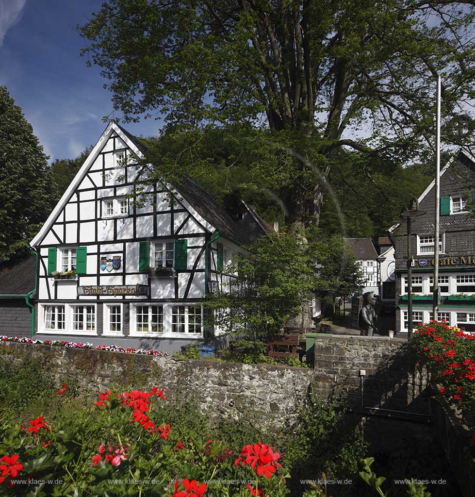 Solingen Unterburg, Schlossbergstrasse,bluehende Geranien im Vordergrund, Burger Brezelbaecker Denkmal, Stadtsparkasse Solingen und Cafe Meyer, Fachwerk- und Schieferhauser, Brezel auf dem Dach von dem Caf; Solingen-Unterburg, Schlossbergstrasse, blooming geranium , Burger pretzel baker historical monument, cafe Meyer, with frame houses and houses of shist, a pretzel is on the roof of the caf