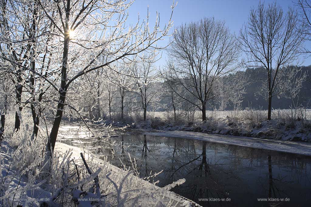 Der Fluss Agger bei Lohmar Wahlscheid an einem eisigen Wintertag verschneit mit Raureif im Gegenlicht mit Sonnenstern; the river Agger at a frosty winder day in snow covered landscape with hoarfrost in trees and gras with sunwhich lokks likes a star