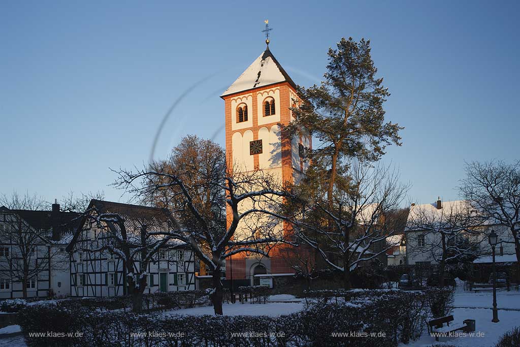 Odenthal Sankt Pankratius Pfarrkirche umgeben von Fachwerkhaeusern im Schnee im waremen Licht der untergehenden Abendsonne; St. Pankratius church with half-timbered houses in the surrounding in warm eveneing sunlight and snow.