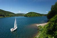 Aggertalsper, Blick von Sueden zur Halbinsel Burg Zinne zwischen dem Agger und Genkelarm, einem Segwelboot und dem Unnenbergturm am Horizont bei klarem Wetter mit blauem Himmel, wenigen Wolken in Fruehsommerlandschaft; Agger dam view over the barrage with a sailboat in summer landscape, Unnenberg look out at the horizon, blue sky few clouds