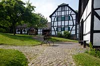 Bergisch Gladbach Bensberg, Bergisches Museum fuer Bergbau Handel und Gewerbe, Blick ueber Kopftsteinplaster Weg zum Backhaus hinten links, Scheune mitte und Handwerkerwohnhaus rechts; Museum of mining and trading