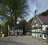 Solingen Unterburg, Schlossbergstrasse, Kopsteinpflasterplatz mit Briefkasten der Deutschen Post AG, Burger Brezelbaecker Denkmal, Stadtsparkasse Solingen und Cafe Meyer, Fachwerk- und Schieferhauser, Brezel auf dem Dach von dem Caf; Solingen-Unterburg, Schlossbergstrasse, a place of cobble stone pavement, with a german letter box, Burger pretzel baker historical monument, cafe Meyer, with frame houses and houses of shist, a pretzel is on the roof of the caf