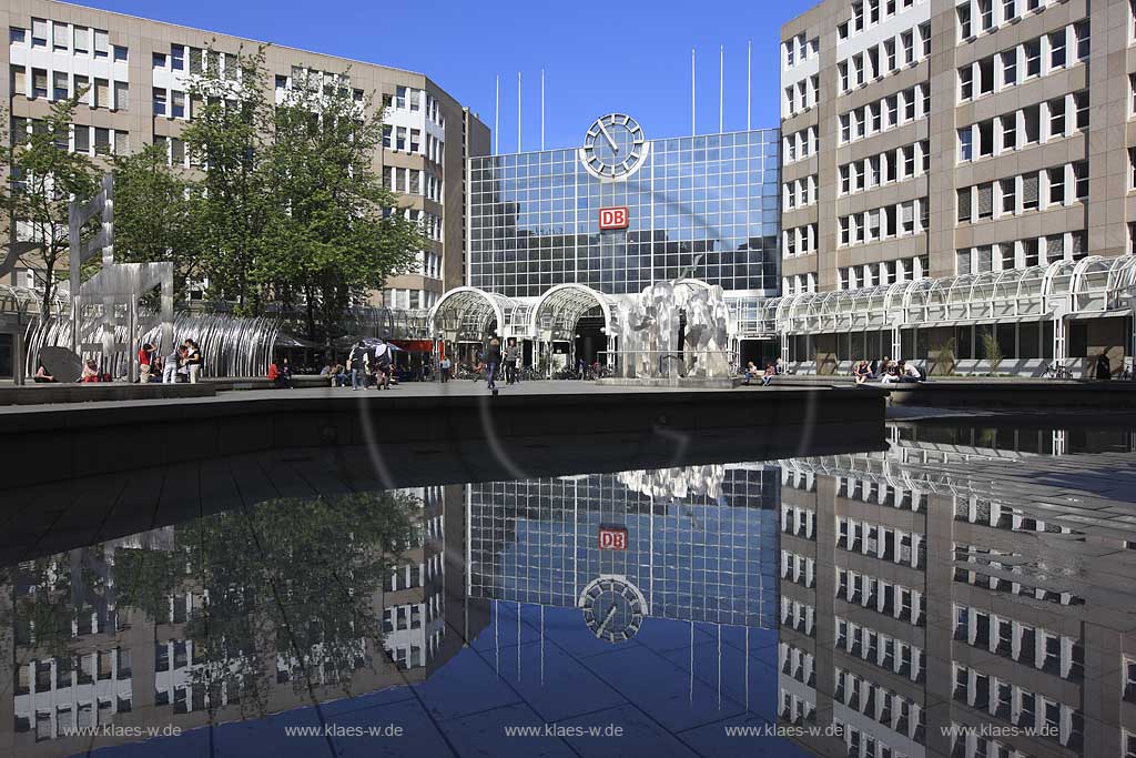 Blick auf den Hauptbahnhof in Dsseldorf, Duesseldorf-Innenstadt mit Sicht auf Skulpturen und Menschen und Spiegelbild vom Bahnhofsgebaeude im Teich