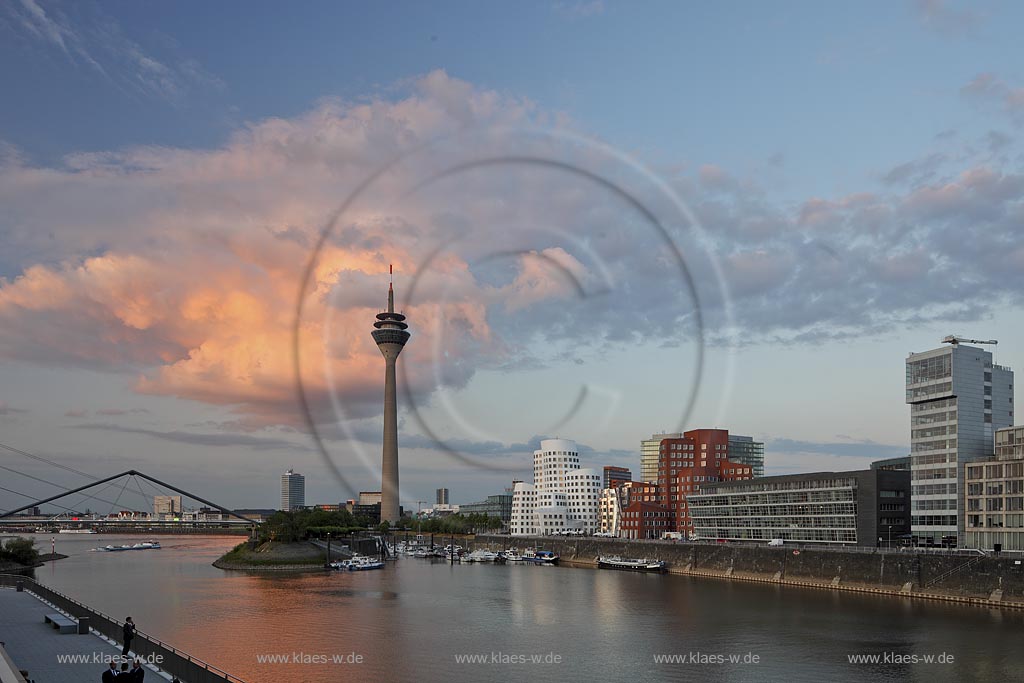 Duesseldorf Hafen, Medienhafen Panoramablick mit Rhein, neuer Fussgaegerbruecke. Rheinturm, 3 Frank O. Gehry Bauten: Zollhof 3 weisse Fassade, Zollhof 2 Spiegelfassade, Zollhof 1, Backsteinfassade,  in Abendstimmung mit roter Wolke, angstrahlt vom Licht der untergehenden Sonne; Duesseldorf-Hafen, mediaport panoramaview with rhine, new pedestrian bridge, rhinetower, Frank O. Gehry buildings duty yard 3 with white facade, duty yard 2 with mirror facade, duty yard 1 with clinker facade  with a red cloud coloured from evening sunset light