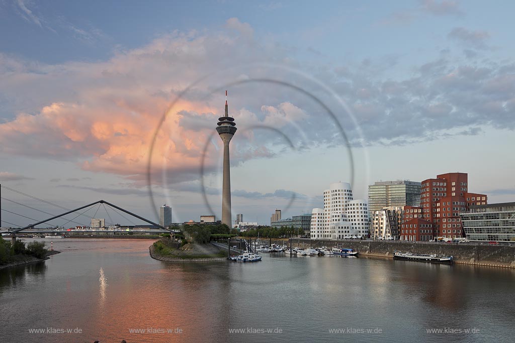 Duesseldorf Hafen, Medienhafen Panoramablick mit Rhein, neuer Fussgaegerbruecke. Rheinturm, 3 Frank O. Gehry Bauten: Zollhof 3 weisse Fassade, Zollhof 2 Spiegelfassade, Zollhof 1, Backsteinfassade,  in Abendstimmung mit roter Wolke, angstrahlt vom Licht der untergehenden Sonne; Duesseldorf-Hafen, mediaport panoramaview with rhine, new pedestrian bridge, rhinetower, Frank O. Gehry buildings duty yard 3 with white facade, duty yard 2 with mirror facade, duty yard 1 with clinker facade  with a red cloud coloured from evening sunset light