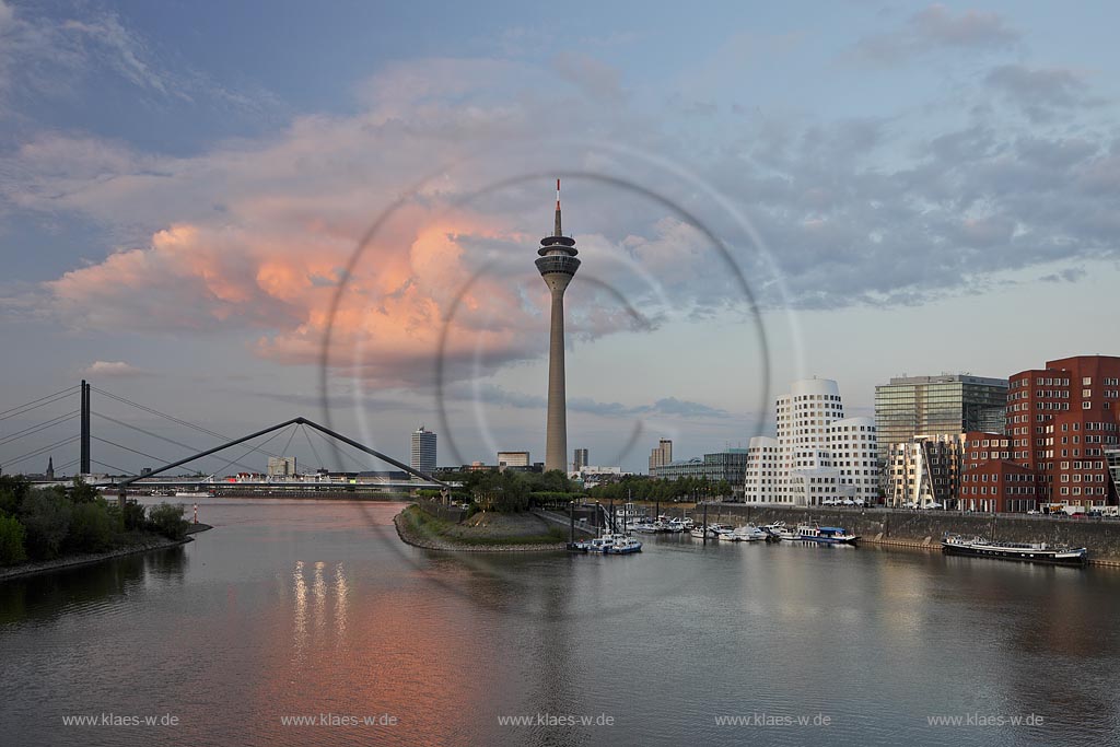 Duesseldorf Hafen, Medienhafen Panoramablick mit Rhein, neuer Fussgaegerbruecke. Rheinturm, 3 Frank O. Gehry Bauten: Zollhof 3 weisse Fassade, Zollhof 2 Spiegelfassade, Zollhof 1, Backsteinfassade,  in Abendstimmung mit roter Wolke, angstrahlt vom Licht der untergehenden Sonne; Duesseldorf-Hafen, mediaport panoramaview with rhine, new pedestrian bridge, rhinetower, Frank O. Gehry buildings duty yard 3 with white facade, duty yard 2 with mirror facade, duty yard 1 with clinker facade  with a red cloud coloured from evening sunset light