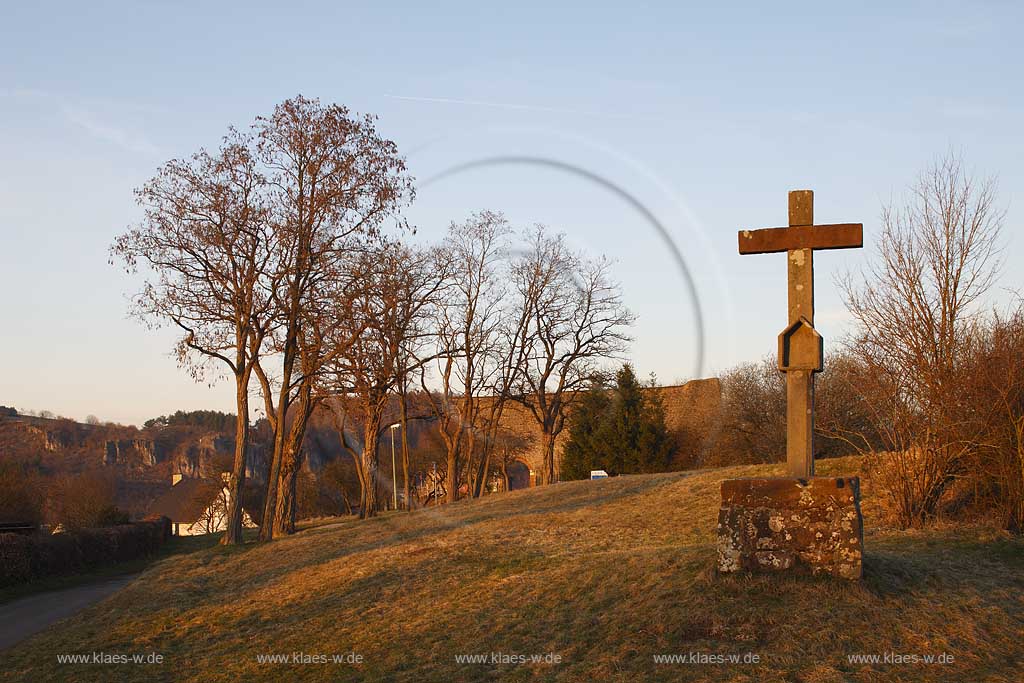 Gerolstein,  Schildmauer der Burgruine Lwenburg, bzw. Burg Gerolstein oder Burg Gerhardstein genannt, mit einem altersgrauen Steinaltar auf dem ein Kreuz steht, von den Gerolsteinern Nikodemuskreuz genannt wird. Es ist das lteste der vielen Wegekreuze um Gerolstein, das Burgkreuz ist gotisch und drfte aus dem 14. oder 15. Jahrhundert stammen hier fotografiert im Abendlicht der ungergehenden sonne im Rcken; Shield wall or ruine of castle Gerolstein with a historical gothic crucifix in the front of ruine in eveing light before sundown