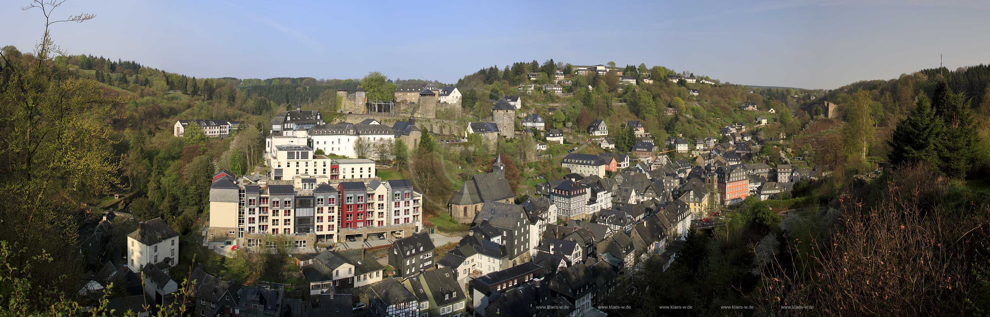 Monschau, extrem Panorama Blick vom Kierberg auf Monschau mit den Markenten Gebaueden von links nach rechts: Burg Monschau, katholische Pfarrkirche Sankt Mariae Geburt und Sankt Josef, Altstadt, evangelische Kirche, Rotes Haus, Haller Ruine im Fruehling; Extreme panorama view from the hill Kierberg to the village Monschau with the castle, catholic church St. Marie born and St. Joseph, old town, evangelic church, red house and Haller ruin