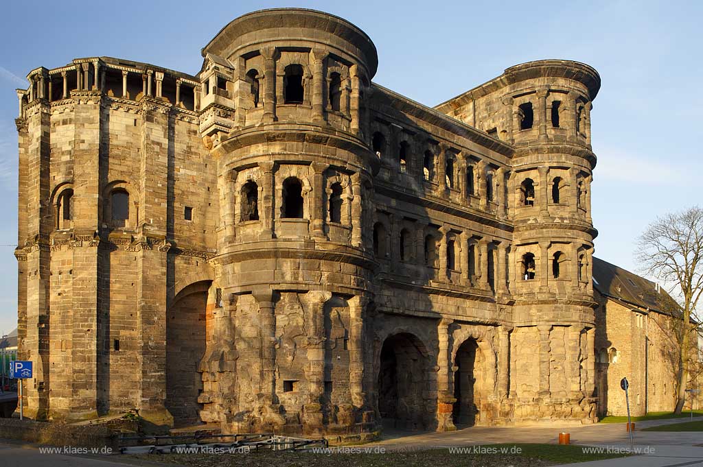 Trier, Ansicht von der Feldseite auf das ehemalige roemische Stadttor Porta Nigra welches zum UNESCO Weltkulturerbe gehoert, Wahrzeichen von Trier fotogriert in den frhen Morgnenstunden nach Sonnenaufgang im warmen gleblichen Sonnnenlicht; View from fieldside to city gate, town gate, town's landmark of Trier early in the morning with warm yellow sunup light