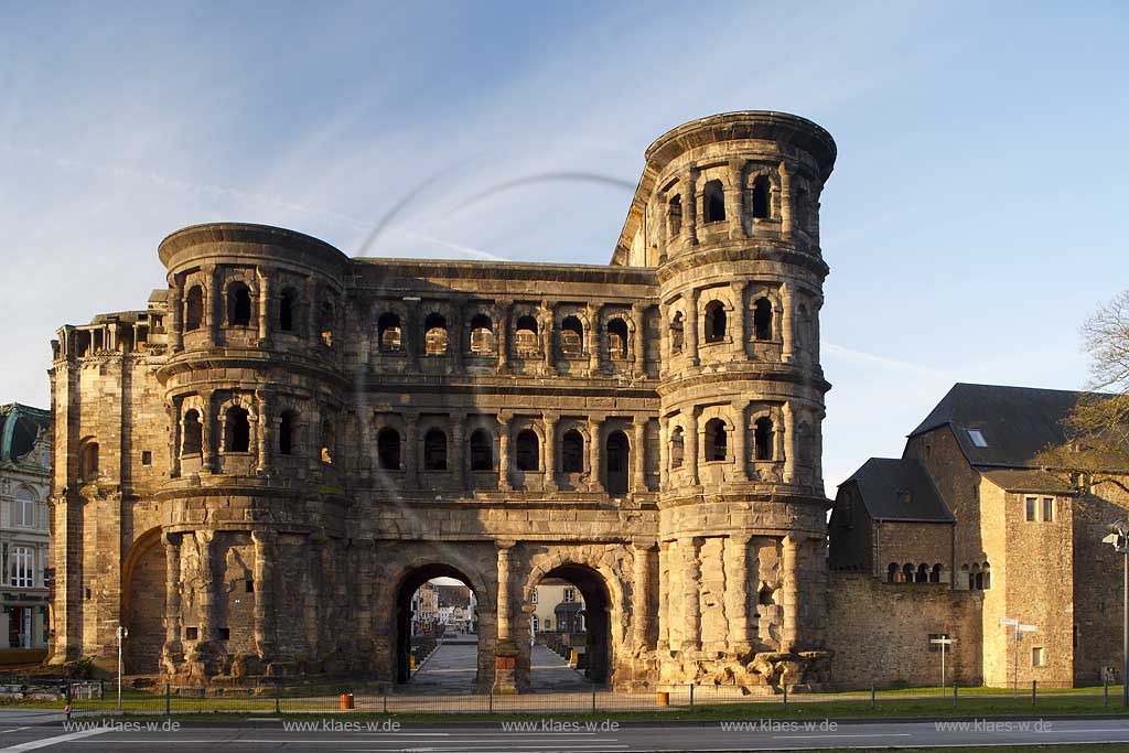 Trier, Ansicht von der Feldseite auf das ehemalige roemische Stadttor Porta Nigra welches zum UNESCO Weltkulturerbe gehoert, Wahrzeichen von Trier fotogriert in den frhen Morgnenstunden nach Sonnenaufgang im warmen gleblichen Sonnnenlicht; View from fieldside to city gate, town gate, town's landmark of Trier early in the morning with warm yellow sunup light