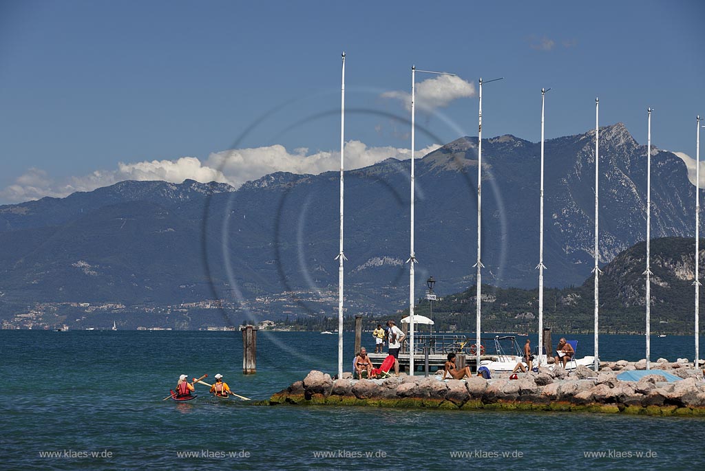 Bardoline Cisano, Blick ueber den Gardasee mit Sonnenbadenden, sich sonnenden Personen gegen das Bergmassiv des Monto Pizzocole; View over Lake Garda with peope bathing in sun against rock mass of mountain Monte Pizzocolo 