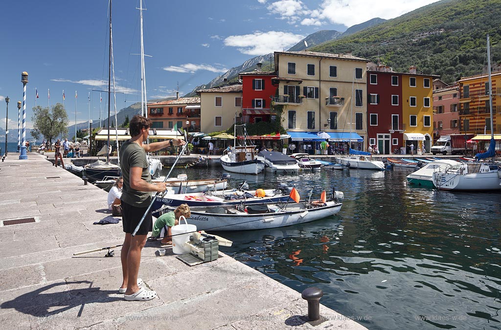 Castelletto Di Brenzone, Blick von der Hafenmole mit Angler ueber Hafen mit Fischerbooten auf bunte Haeuser; Castelletto Di Brenzone, view from the mole with angler over the port with fishing boats to old prettily pointed houses