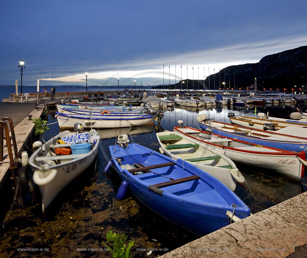 Garda Blick ueber Hafen mit bunten Fischerbooten und Hafenmole in Abendstimmung mit Wolkenhimmel; Garda view over port with colourful fishing boats and mole in atmosheric evening light, cloudy