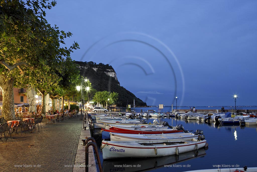 Garda Blick von der Promenade mit Hafen, bunten Fischerbooten und Mole zum Rocca di Garda waehrend der blauen Stunde; Garda view from the promenade over port with colourful fishing boats and mole to the mountain Rocca di garda during blue hour