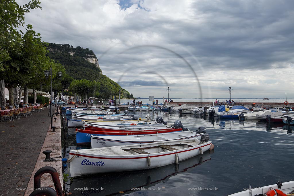 Garda Blick von der Promenade mit Hafen, bunten Fischerbooten und Mole zum Rocca di Garda in Wolkenstimmung; Garda view from the promenade over port with colourful fishing boats and mole to the mountain Rocca di garda in cloudy atmosphere