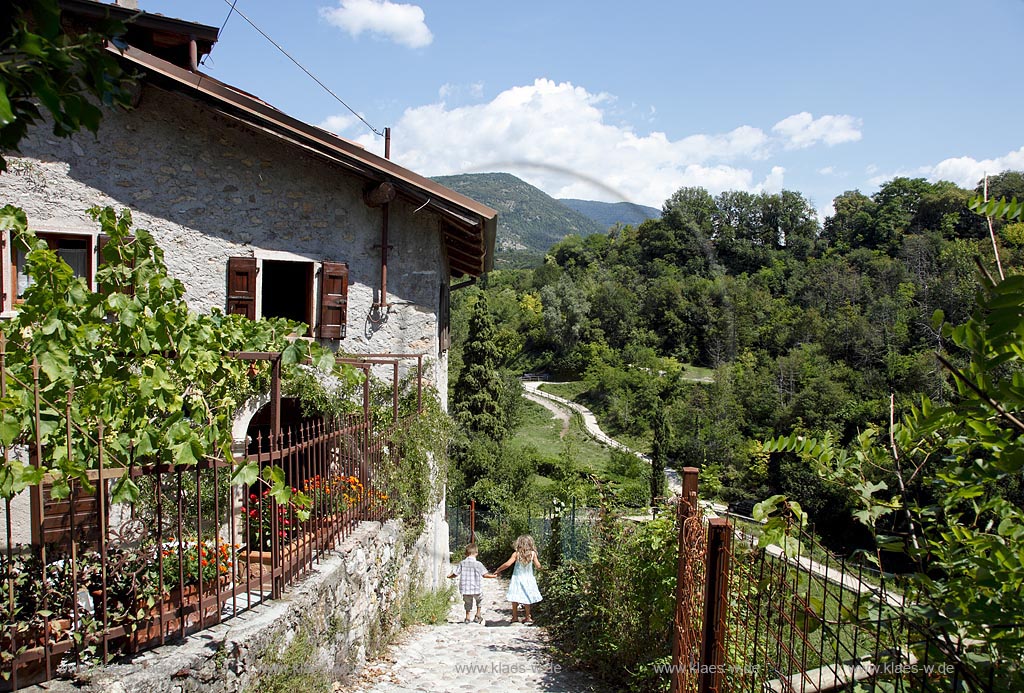 Garda Wanderweg vorbei an einem alten Steinhaus mit Natursteinmauer und Natursteinpflaster im Tal der Muehlen in Sommerlandschaft; Garda hiking path with an old stone house in the yvalley of mills; Garda Val dei Mulini