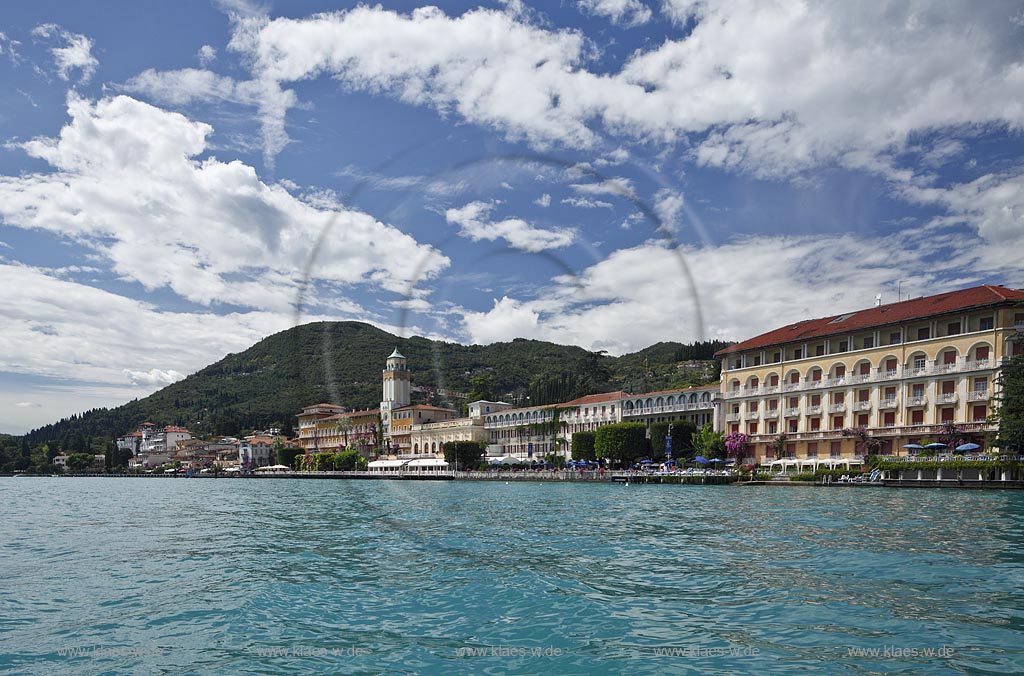 Gardone Riviera, Panoramablick vom Gardasee aus auf den Ort, Seeseite mit Seepromenade und den modernen Hotels dahinter der Monta San Bartolomeo, Wolkenstimmung; Gardone Rivera, view from lake Garda to the town with promenade in front of elegant late 19th century hotels, in backgrount mountain Monte St. Bartolomeo, atmospheric clouds; Gardone Riviera il lungolago davanti agli eleganti hotel di fine ottocento