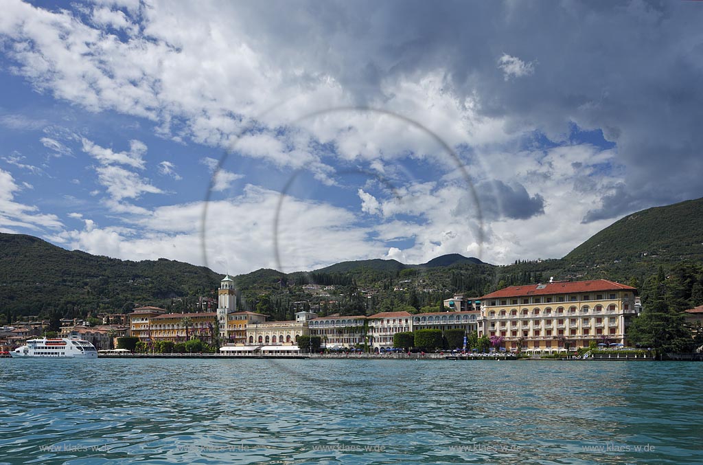 Gardone Riviera, Panoramablick vom Gardasee aus auf den Ort, Seeseite mit Seepromenade und den modernen Hotels dahinter der Monta San Bartolomeo, Wolkenstimmung; Gardone Rivera, view from lake Garda to the town with promenade in front of elegant late 19th century hotels, in backgrount mountain Monte St. Bartolomeo, atmospheric clouds; Gardone Riviera il lungolago davanti agli eleganti hotel di fine ottocento