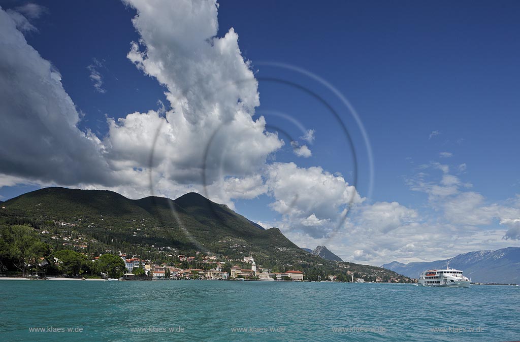 Gardone Riviera, Panoramablick vom Gardasee aus auf den Ort, Seeseite mit Seepromenade und den modernen Hotels, rechts das Luxus Motorschiff Andromeda Baujahr 2007 der Schiffahrtsgesellschaft Navigarda, im Hintergrund von links nach rechts Monte Pizzocolo, Monte Castello, Monte Baldo, extreme Wolkenstimmung; Gardone Rivera, view from lake Garda to the town with promenade in front of elegant late 19th century hotels, right side the the modern motorship Andromeda launched 2007, in the backgrond from left to right mountain Monte Pizzocole, Monte Castello, Monte Baldo, extreme atmospheric clouds; Gardone Riviera il lungolago davanti agli eleganti hotel 