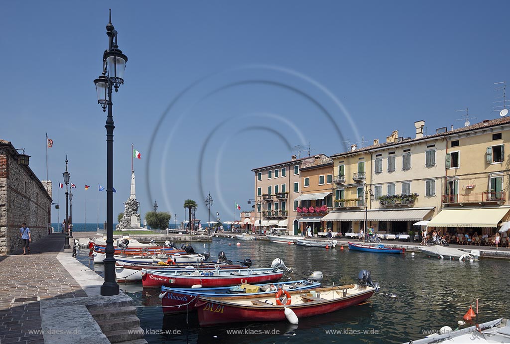 Lazise, Blick ueber den Hafen Richtung Gardasee mit bunten Fischerbooten und Haeusern sowie dem Denkmal fuer Kriegsgefallene; Lazise, view over the port with colourfull fishing boats, houses and war victim memoirial 