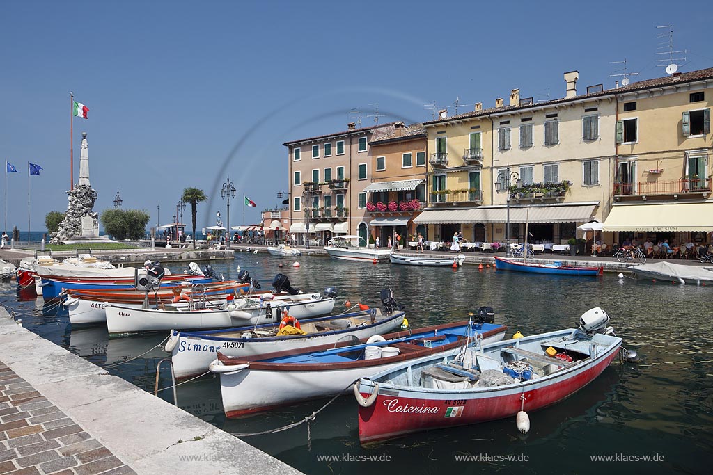 Lazise, Blick ueber den Hafen Richtung Gardasee mit bunten Fischerbooten und Haeusern sowie dem Denkmal fuer Kriegsgefallene; Lazise, view over the port with colourfull fishing boats, houses and war victim memoirial 