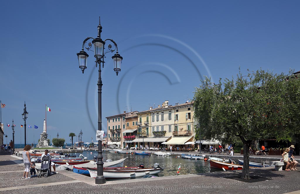 Lazise, Blick ueber den Hafen Richtung Gardasee mit bunten Fischerbooten und Haeusern sowie dem Denkmal fuer Kriegsgefallene; Lazise, view over the port with colourfull fishing boats, houses and war victim memoirial 
