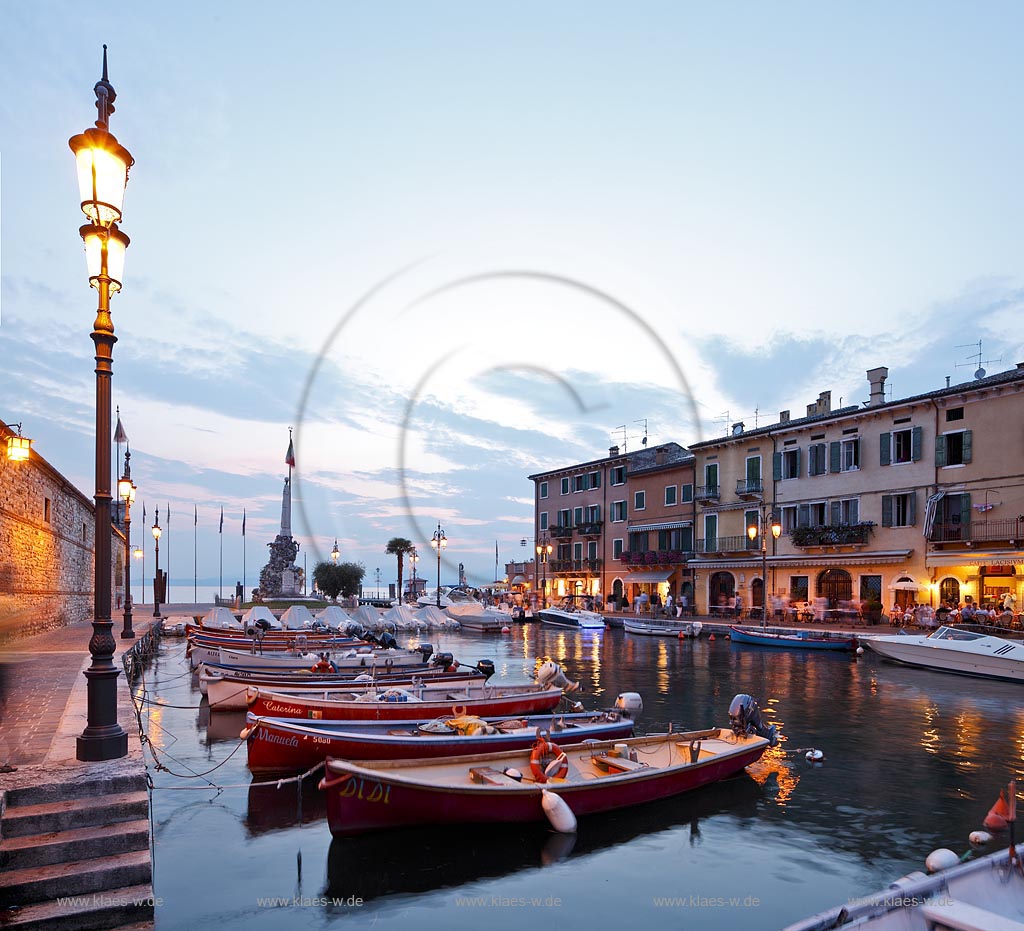 Lazise, Blick ueber den Hafen Richtung Gardasee mit bunten Fischerbooten und Haeusern sowie dem Denkmal fuer Kriegsgefallene zur blauen Stunde; Lazise, view over the port with colourful fishing boats, houses and war victim memoirial during blue hour