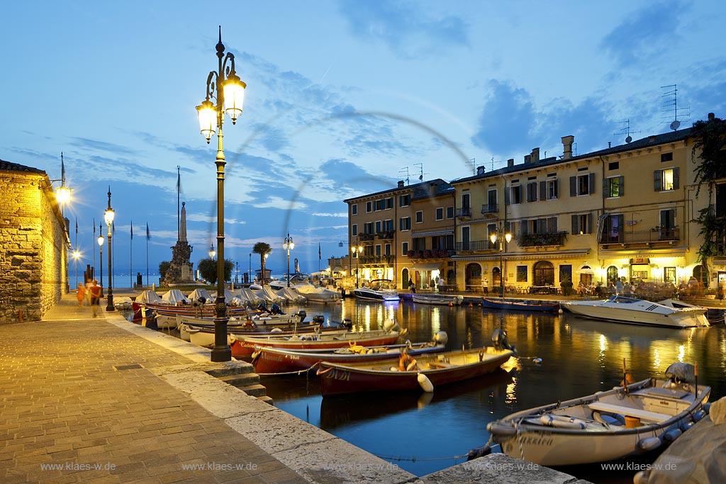 Lazise, Blick ueber den Hafen Richtung Gardasee mit bunten Fischerbooten und Haeusern sowie dem Denkmal fuer Kriegsgefallene zur blauen Stunde; Lazise, view over the port with colourful fishing boats, houses and war victim memoirial during blue hour