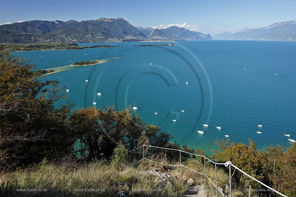 Manerba del Garda, Blick von Rocca di Manerba ueber den Gardasse in nordwestliche Richtung mit Bergkette des Monte Pizzocolo und Monte Castello di Gaino, Motorboote auf dem See fahrend und liegend, Isola di San Biagio Mitte links und Isola del Garda mit Villa Borghese dahinter Mitte; Manerba del Garda, a clear view from Rocca di Manerba onto Lake Garda to the northwest line of sight, motorboats on the lake.