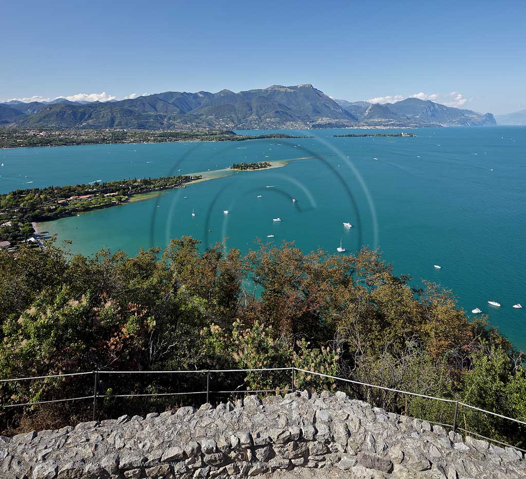 Manerba del Garda, Blick von Rocca di Manerba ueber den Gardasse in nordwestliche Richtung mit Bergkette des Monte Pizzocolo und Monte Castello di Gaino, Motorboote auf dem See fahrend und liegend, Isola di San Biagio Mitte und Isola del Garda mit Villa Borghese dahinter rechts; Manerba del Garda, a clear view from Rocca di Manerba onto Lake Garda to the northwest line of sight, motorboats on the lake.