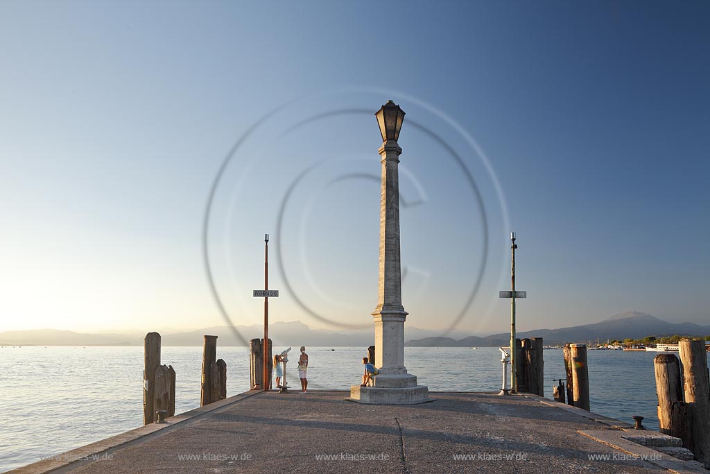 Peschiera, Abenstimmung mit Blick ueber die Hafenmole mit Leuchtmast und Frau mit Kindern zum Gardasee im stimmungsvollen Abendlicht der untergehenden Sonne; Peschiera view over the mole with lightmast in evening sunset light