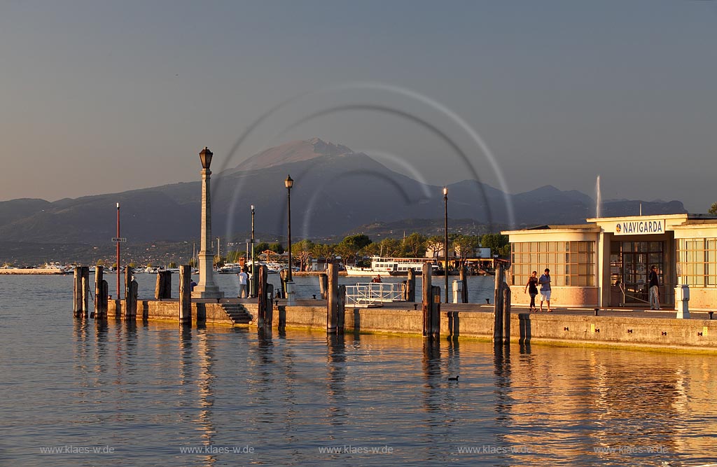 Peschiera, Abenstimmung mit Blick ueber die Hafenmole mit Leuchtmast zum Gardasee im stimmungsvollen Abendlicht der untergehenden Sonne, im Hintergrund der Monte Baldo; Peschiera view over the mole with lightmast in evening sunset light, in the background mountain of Monte Baldo