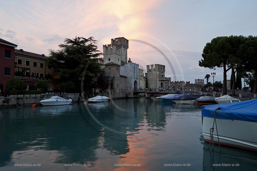 Sirmione, Blick vom Hafen mit Motorbooten zur Scaliger Burg im Licht der untergehenden Abendsonne, rote Wolken vor blauem Himmel; Sirmione, view from port with motorboats to the Scaliger castle during sunset light with red lighted clouds in the blue sky