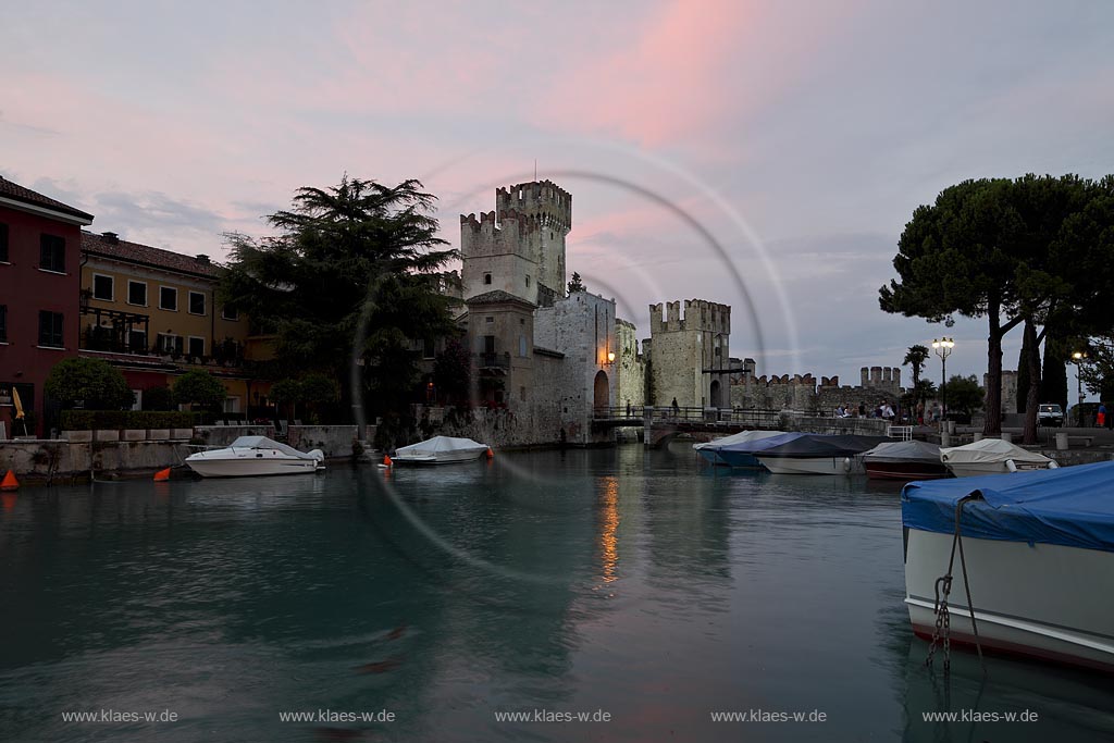 Sirmione, Blick vom Hafen mit Motorbooten zur Scaliger Burg im Licht der untergehenden Abendsonne, rote Wolken vor blauem Himmel; Sirmione, view from port with motorboats to the Scaliger castle during sunset light with red lighted clouds in the blue sky