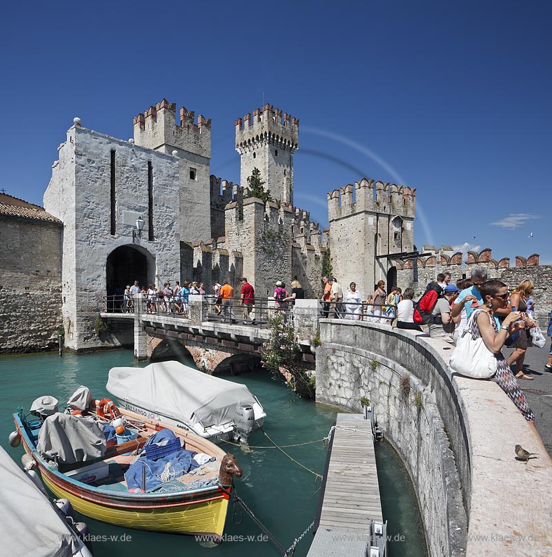 Sirmione, Blick vom Hafen zur Scaliger Burg mit Mauer im Vordegrund auf der ein Haussperling sitz, dahinter Menschen, Touristen, besucher; ; Sirmione, view from port to the Scaliger castle