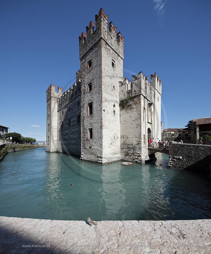 Sirmione, Nahaufnahme der Scaliger Burg, im Vordergrund eine Mauerbruestung mit Haussperling der die Szenerie neugierig zu betrachten scheint; Sirmione, closeup of the Scaliger castle with a house sperrow in the front of picture