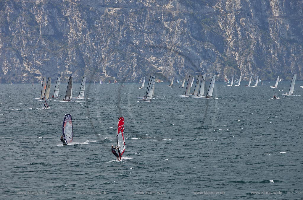 Torbole sul Garda, Surfern auf dem Gardasee bei stuermischem Wind, im Hintergrund Segelkatamaran Regatta vor schroffen Felswaenden; Torbole sul Garda, Lake Garda with wind surfers, windy, in the background a sail catamaran regata and rocks mass