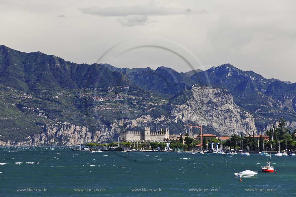 Torri del Benaco, Blick ueber den Gardasee bei Sturm mit Wellengang zur Scaliger Burg, im Hintergrund das Bergpanorama mit der Hochebene von Tignale und Tremosine; Torri del Benaco, view over lake Garda with waves on a stormy day to the Scaliger castle, in the Background the panorama of mountains with tableland of Tignale and Tremosine